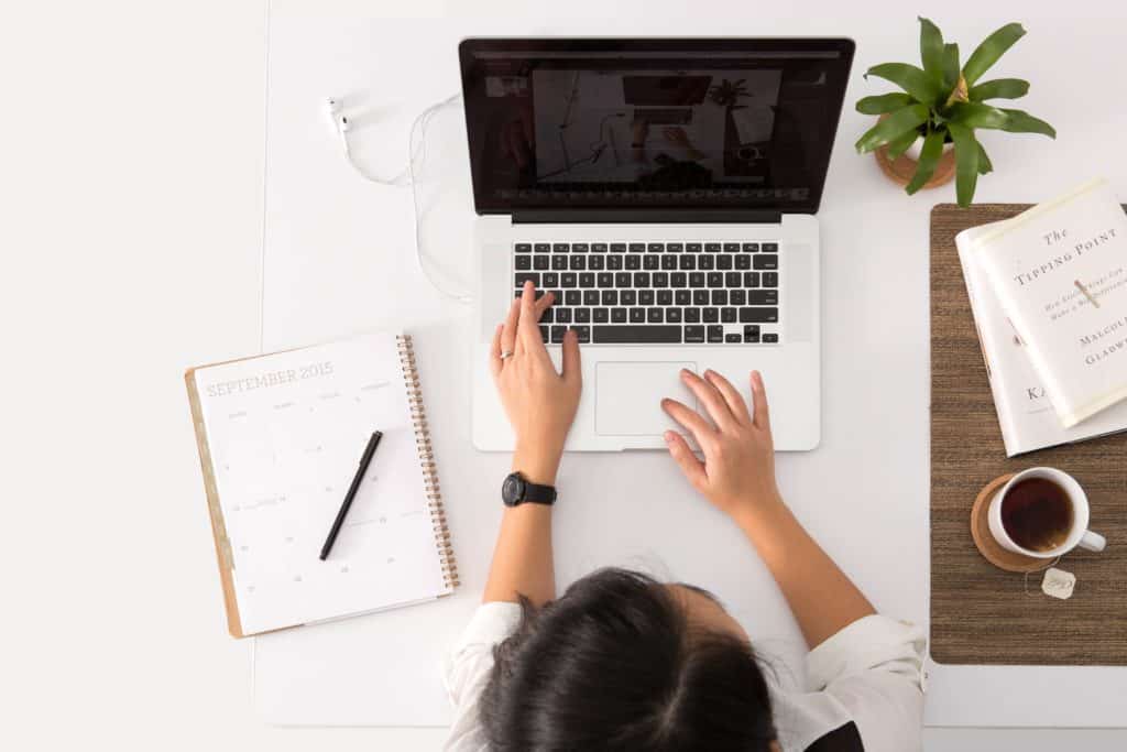 a photo of a girl working at a desk with a laptop and a notepad