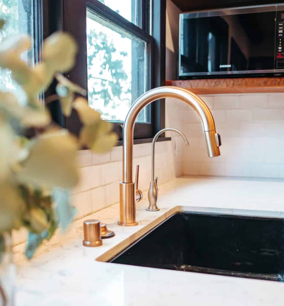 A photo of a kitchen sink, white counter, and a brass faucet